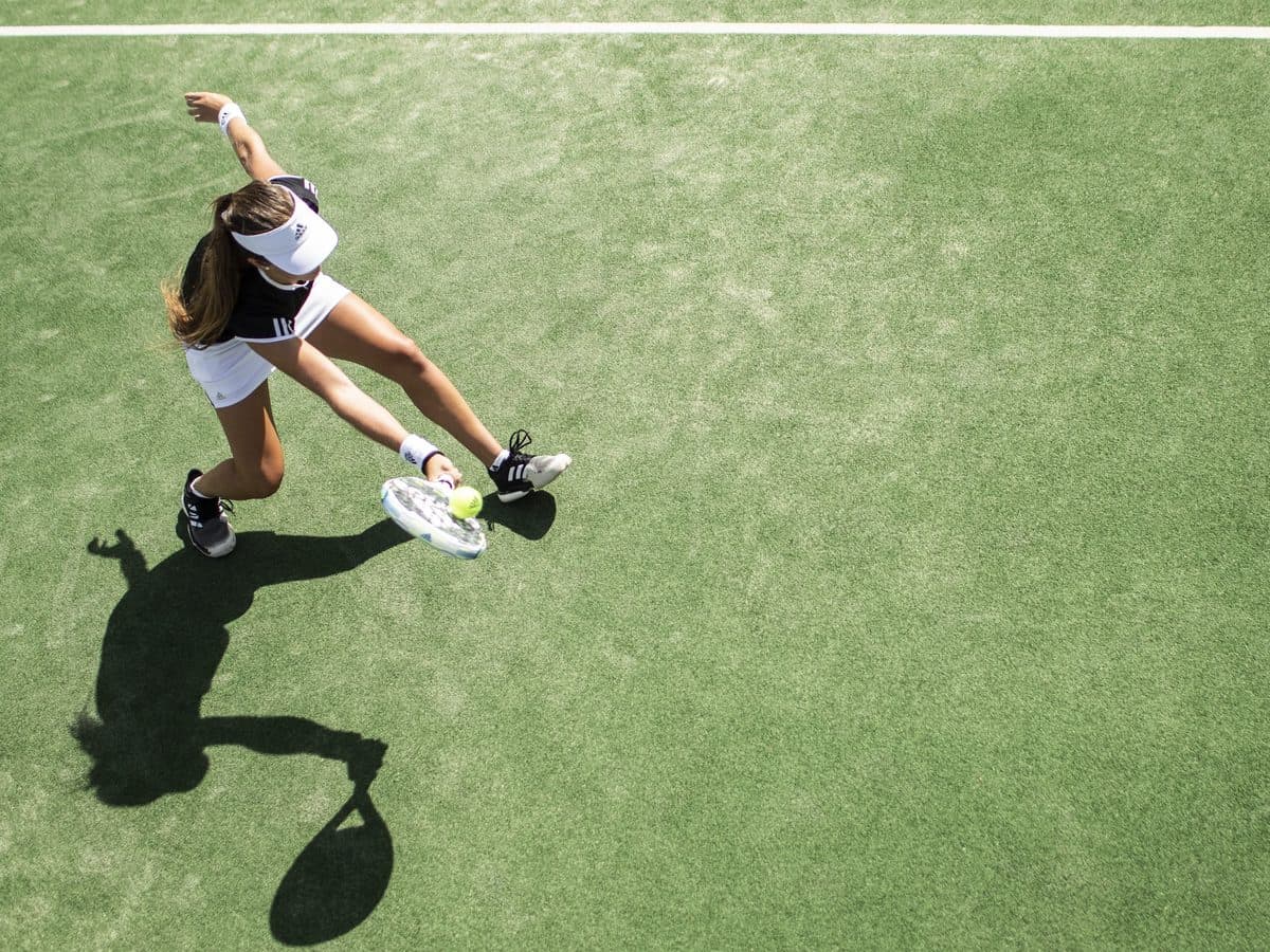 Vue plongeante d’une joueuse de tennis frappant la balle sur un court en gazon synthétique.